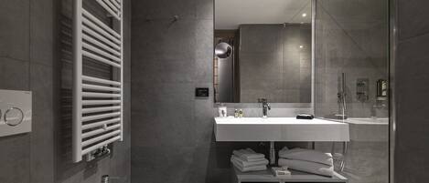 A modern bathroom with a white sink, a mirror, a towel rack, and a shower area.