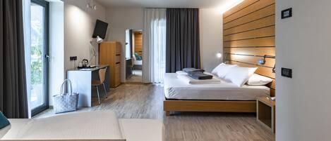 A modern hotel room with a bed, bedside table, desk, chair, and a view of the outdoors.