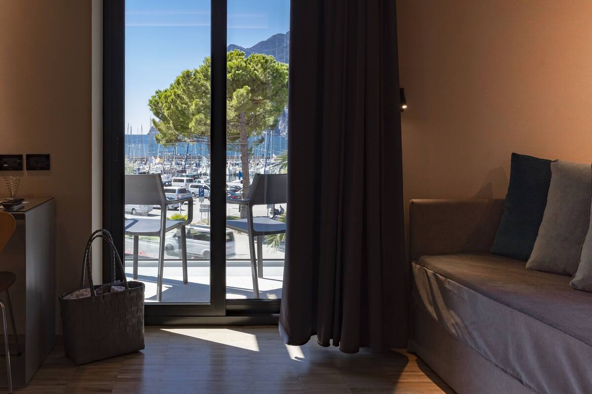 A modern hotel room with a large window, a sofa, a small table, and a chair.