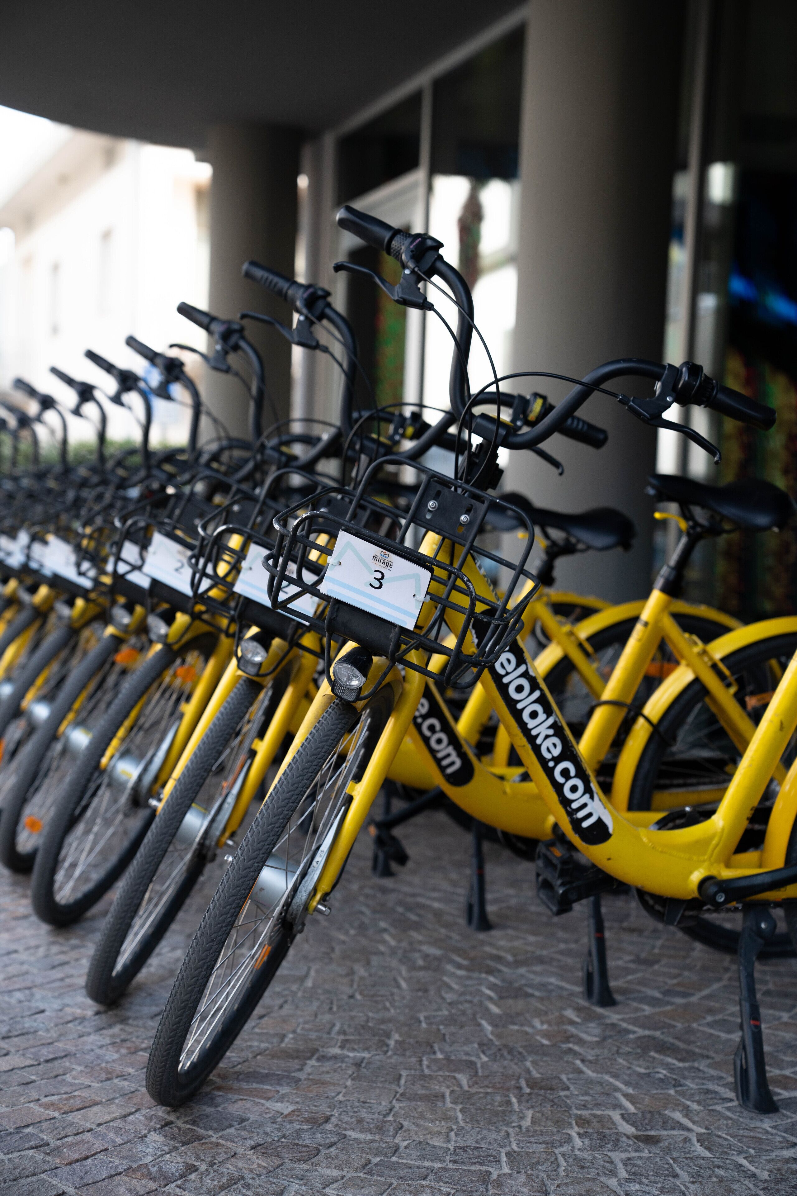 Een rij gele fietsen geparkeerd in een overdekte ruimte met een geplaveid vloertje.