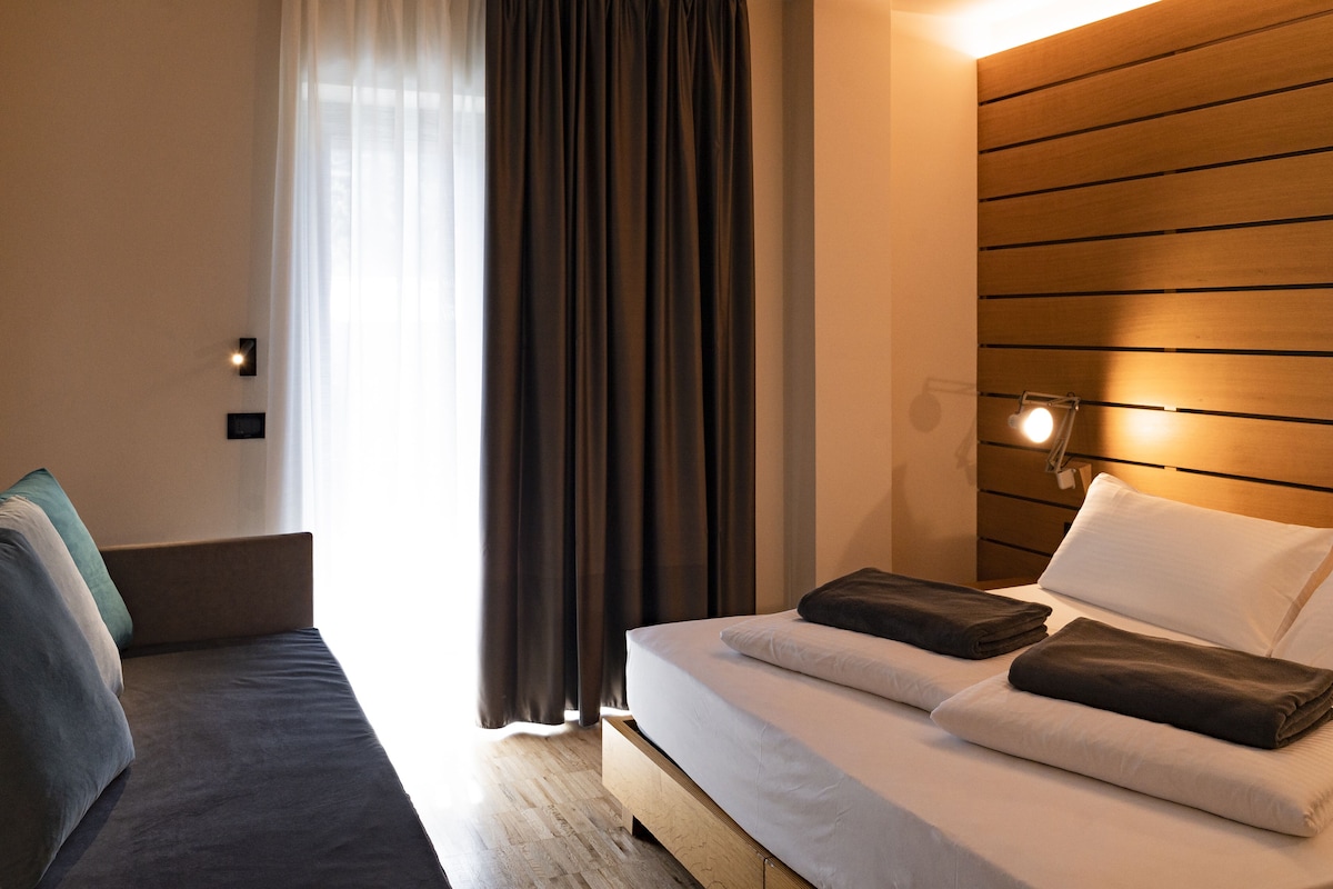 Una habitación de hotel moderna con cama, sofá y cabecera de madera.