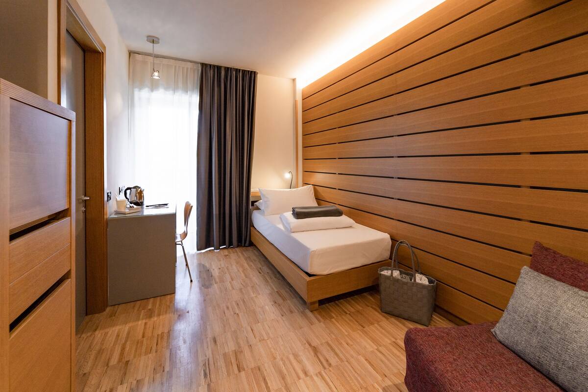A modern hotel room with a wooden bed, a small desk, and a seating area.