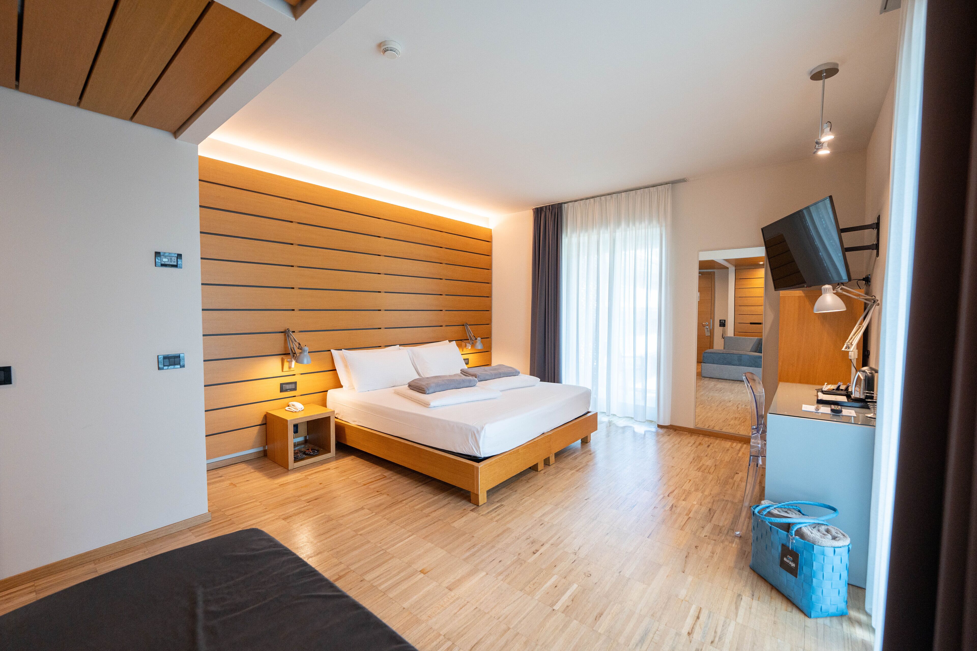 Una habitació d'hotel moderna amb un llit de fusta, taules de nit, un escriptori amb una làmpada i una televisió.