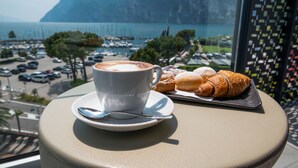 En kop kaffe og en croissant på et bord med udsigt over en lysthavn og bjerge.