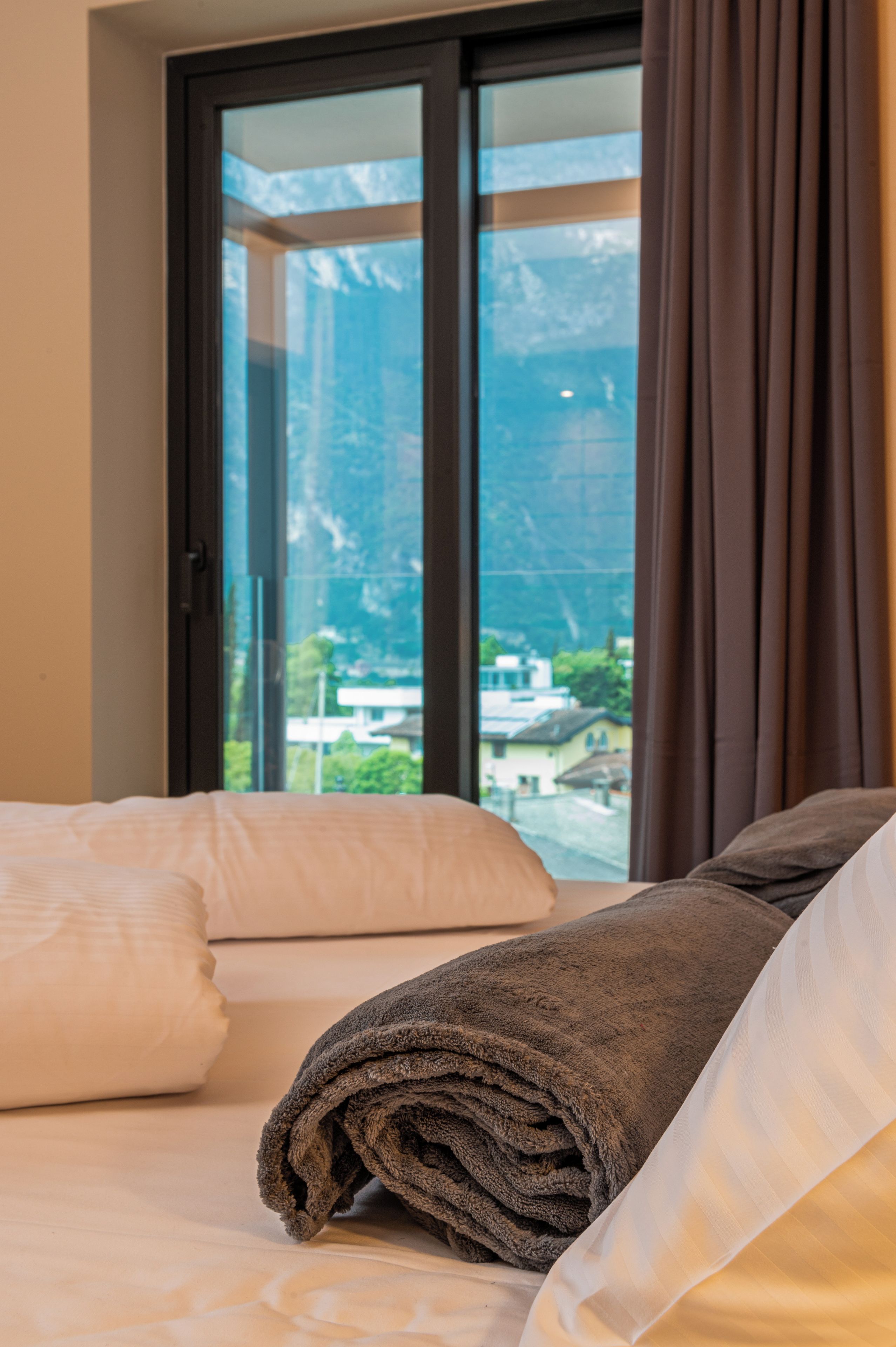 A hotel room with a bed, a window with curtains, and a view of a mountain and buildings.