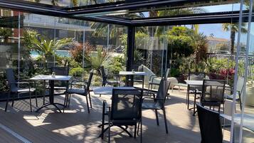 Un patio al aire libre con paredes de vidrio, suelo de madera, sillas y mesas de metal.