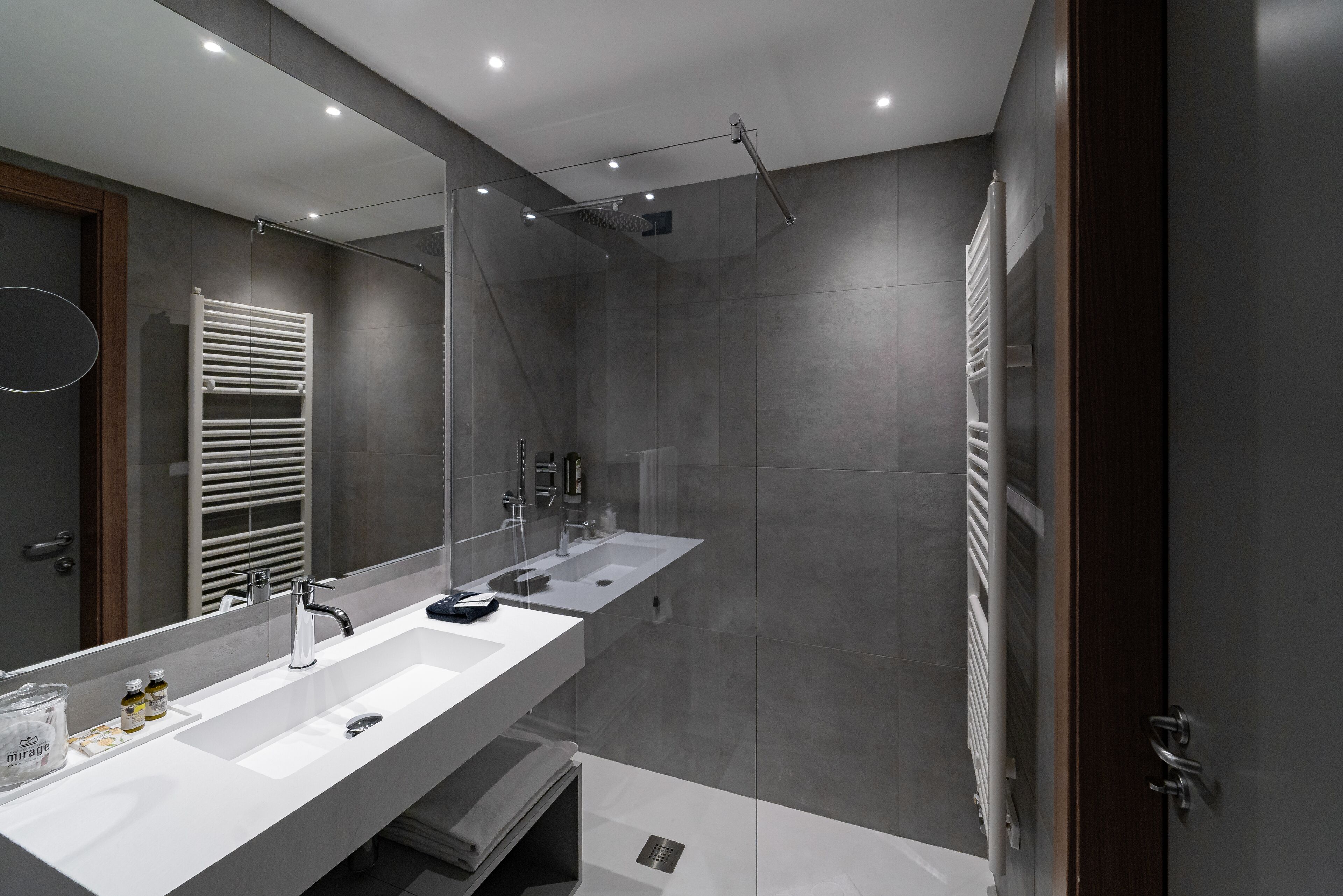 A modern bathroom with a large mirror, dual sinks, a shower, and a towel rack.
