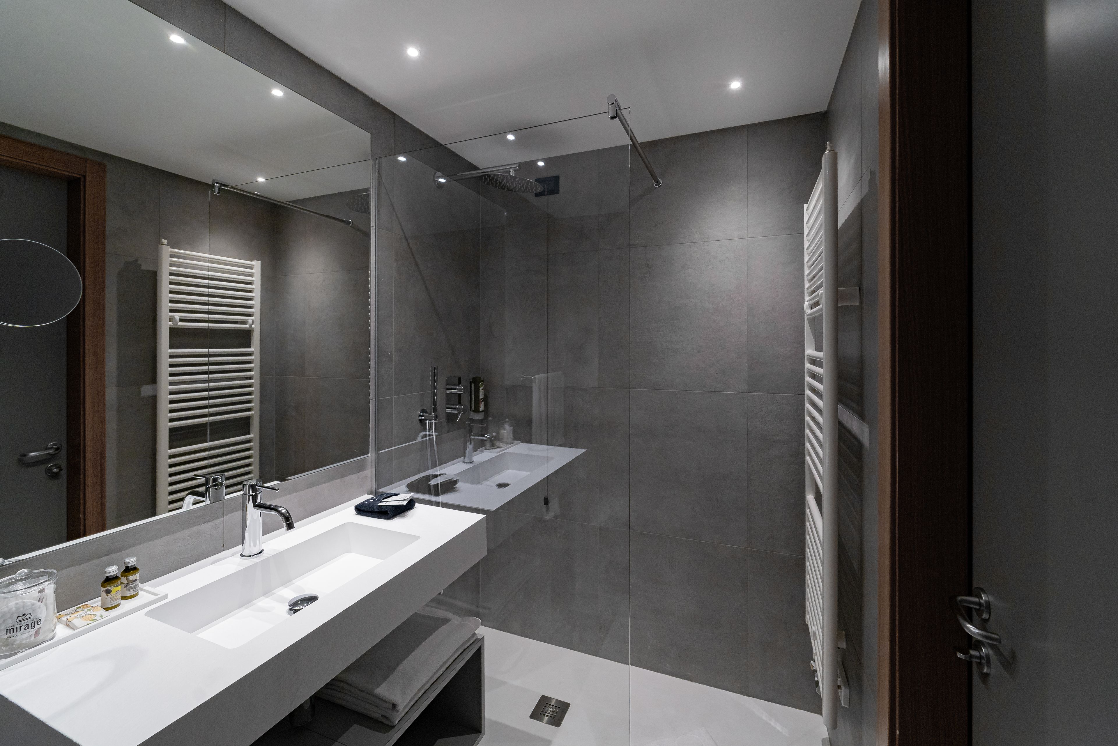 A modern bathroom with a large mirror, dual sinks, a shower, and a towel rack.
