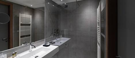 A modern bathroom with a large mirror, dual sinks, a shower, and a towel rack.