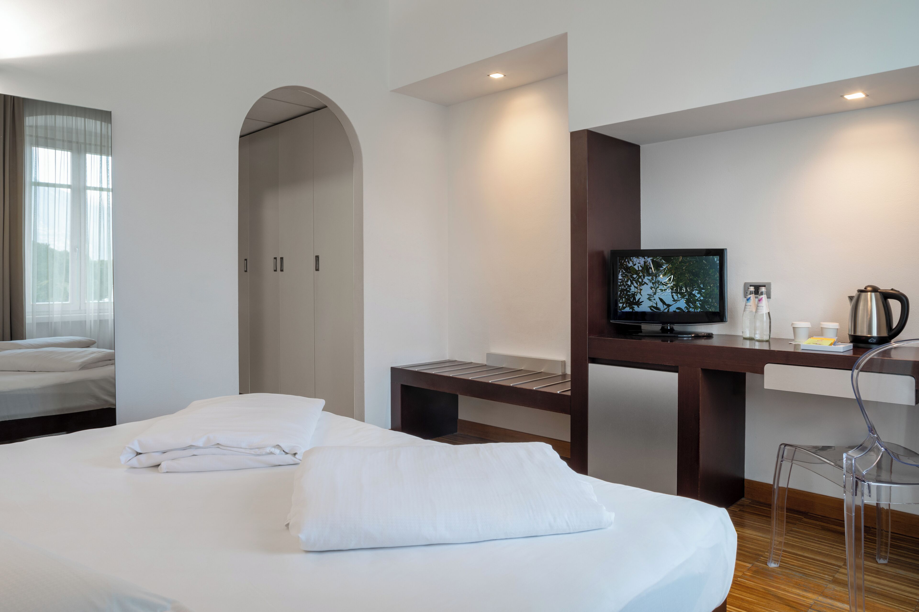 A hotel room with a bed, a desk with a television, a coffee maker, and a chair.