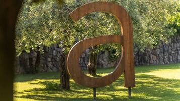 Una gran escultura de madera del número 6 en un parque, con un muro de piedra y árboles al fondo.