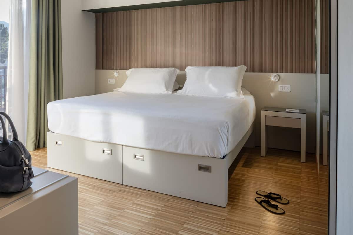 A hotel room with a bed, bedside table, and a suitcase on the floor.