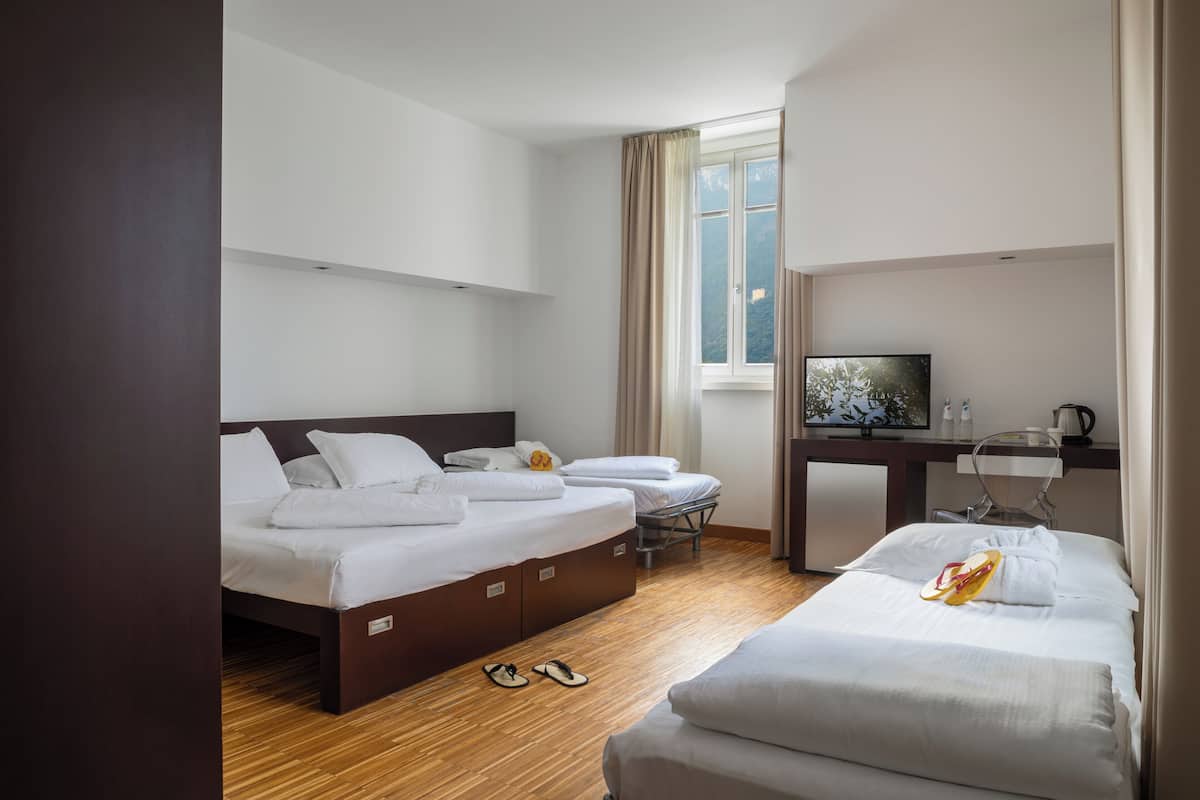 A hotel room with two beds, a desk, a TV, and a window with curtains.