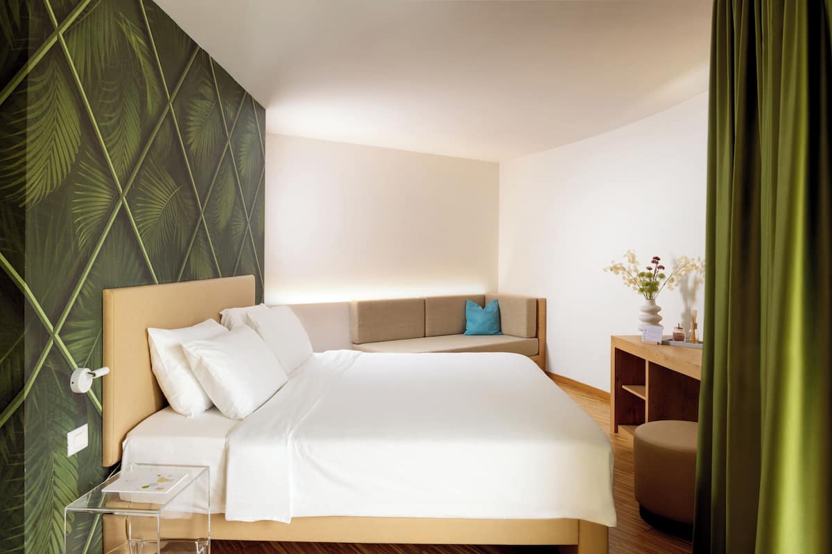 A modern bedroom with a bed, a sofa, a wooden side table, and a green curtain.