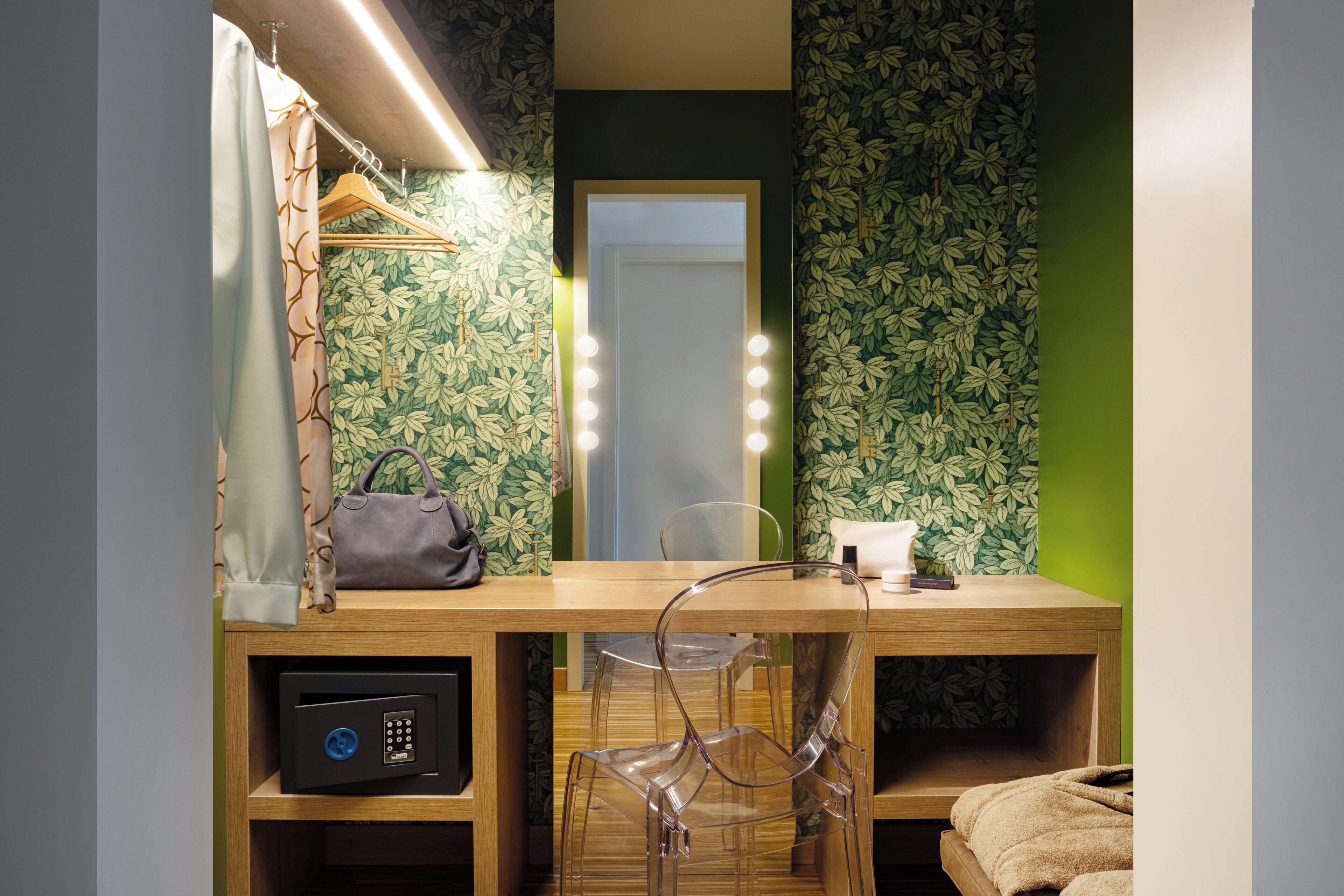 Un baño con tocador, espejo con luces, toalla y papel tapiz floral verde.