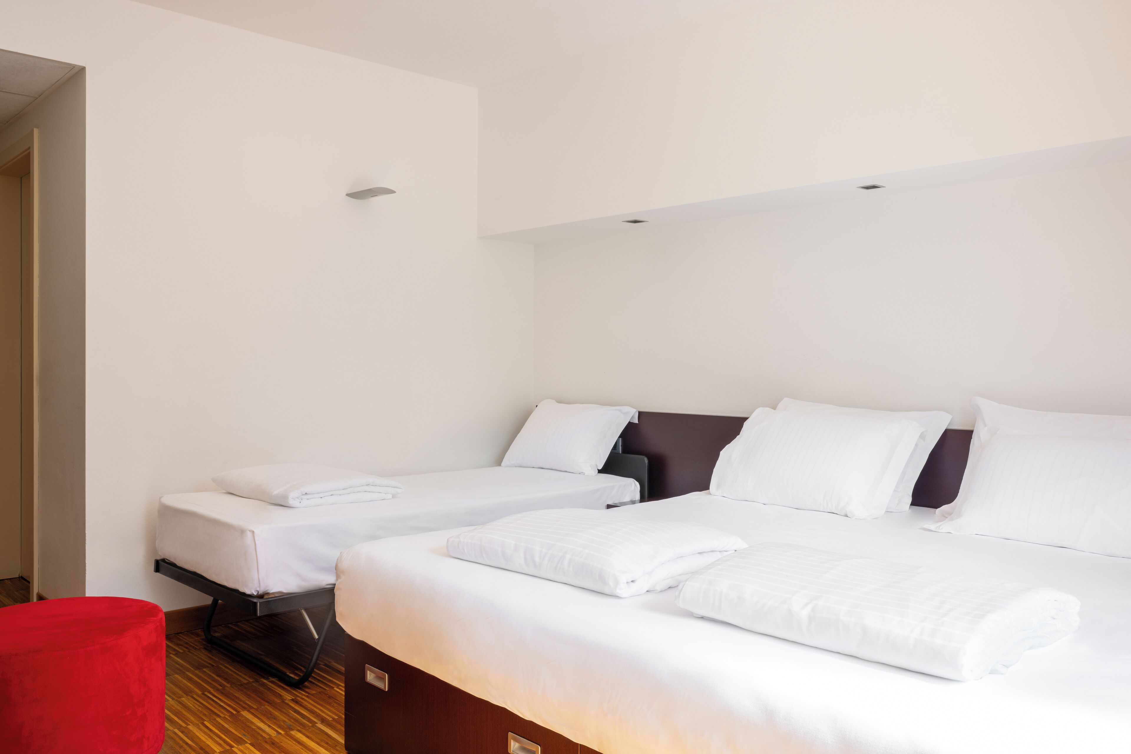 Una habitación de hotel con dos camas, una silla roja y piso de madera.