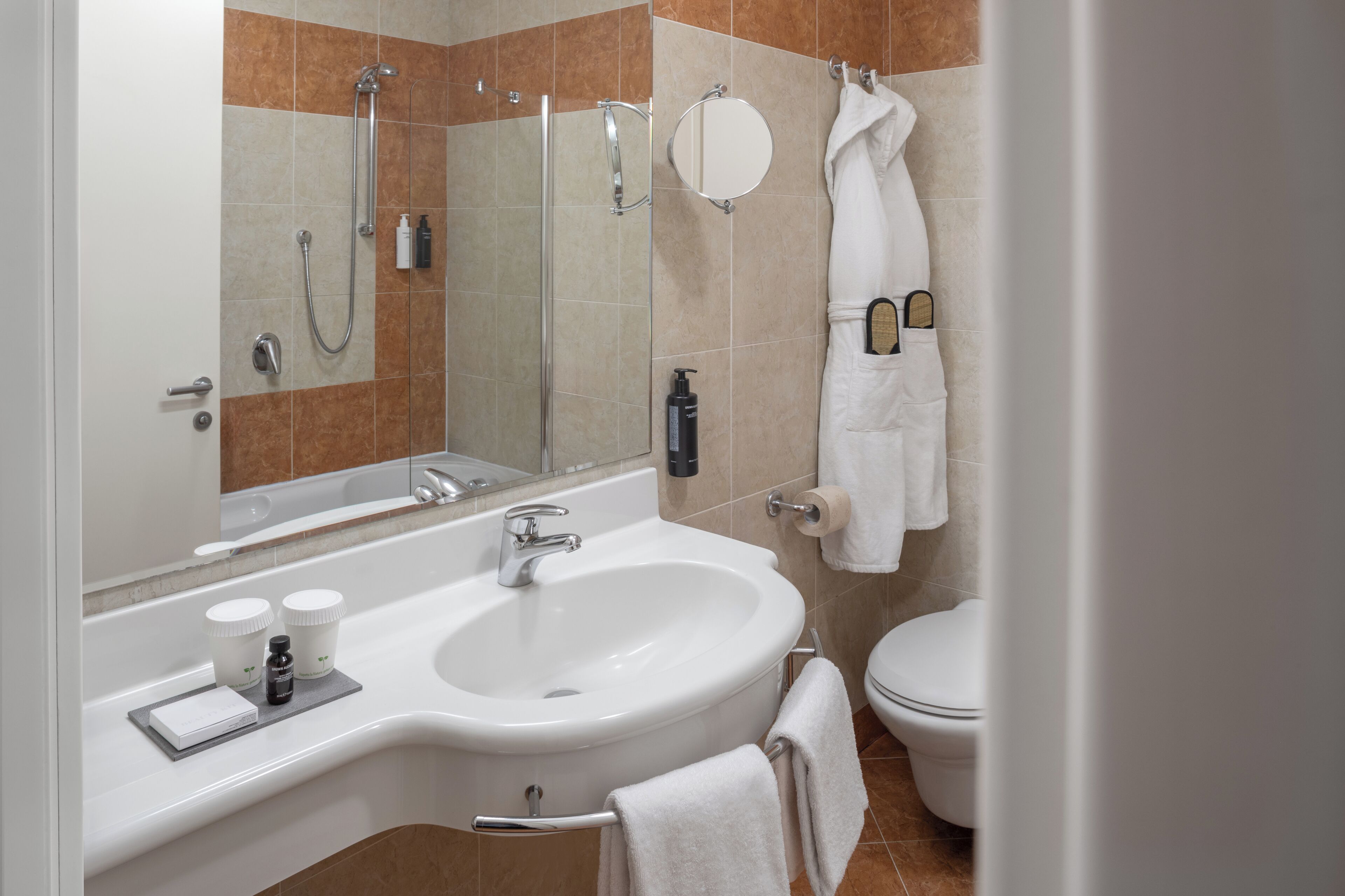 Un baño moderno con un espejo grande, una bañera, un lavamanos y un inodoro.