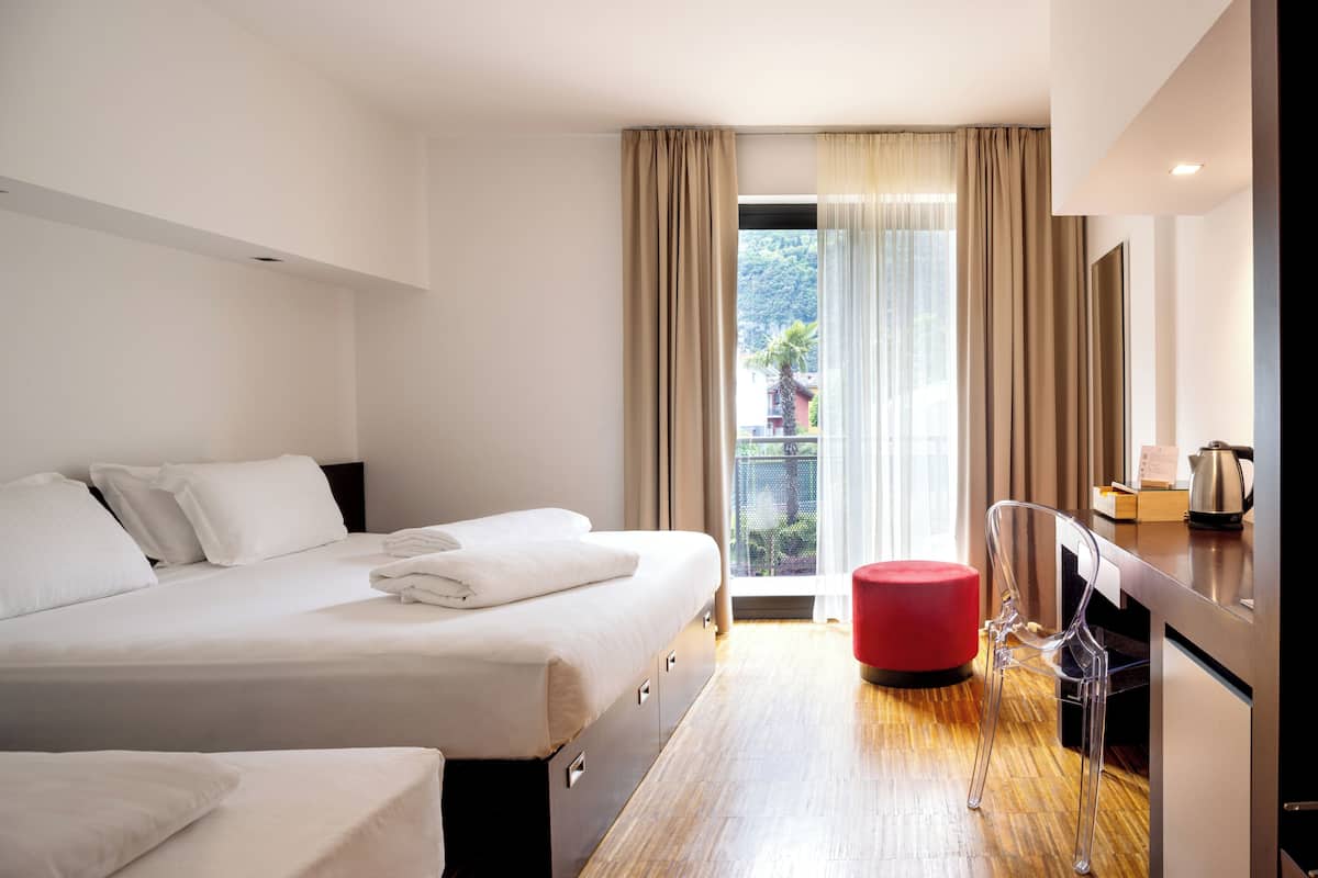 A modern hotel room with a large bed, a small desk, and a red ottoman.