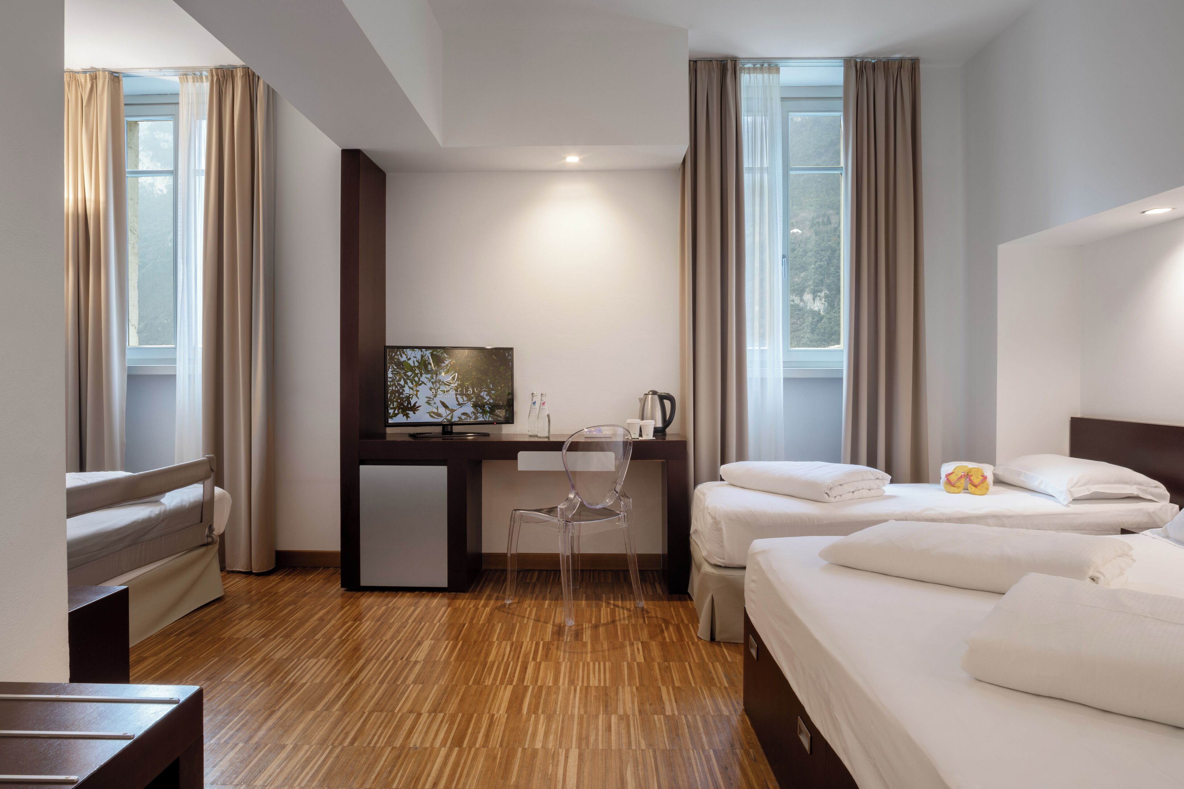 Ein Hotelzimmer mit zwei Betten, einem Schreibtisch mit Fernseher, einem Sessel und einer Kaffeemaschine.