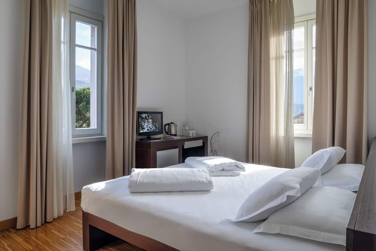 A hotel room with a bed, a desk with a computer, and a window with curtains.
