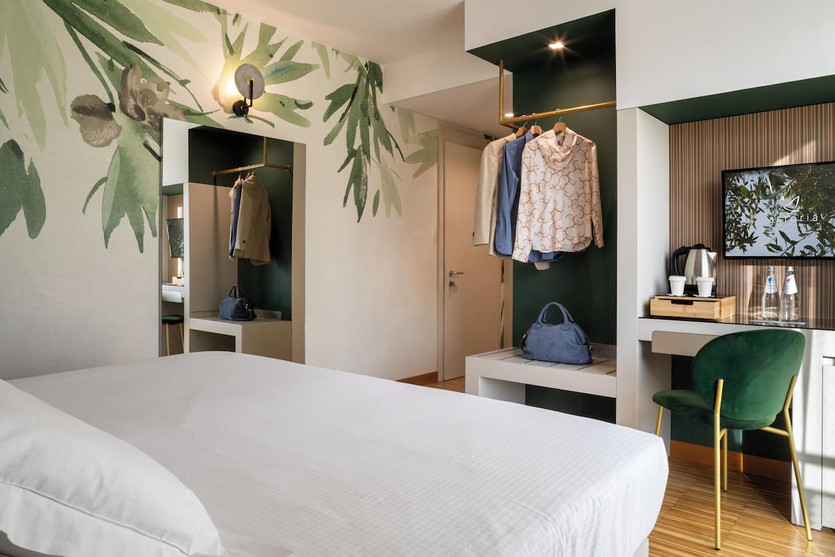 A hotel room with a bed, a desk with a chair, a wardrobe, and a television.