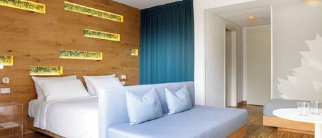 Ein modernes Hotelzimmer mit einer Wand in Holzoptik, einem großen Bett mit weißer Bettwäsche, einem blauen Sofa und einem kleinen Tisch mit Gläsern.