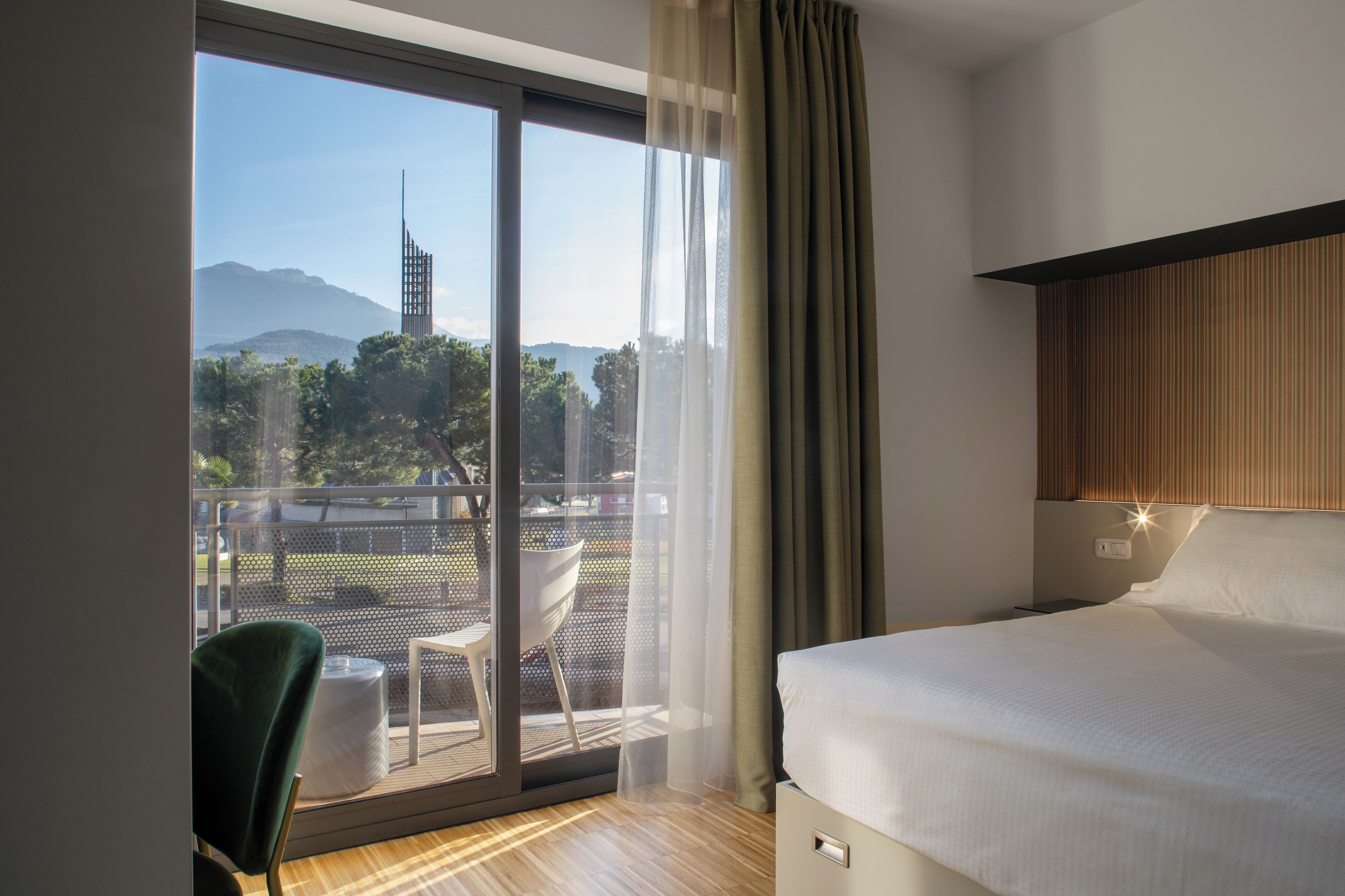 Quarto de hotel com uma cama grande, vista para montanhas e varanda com cadeira e mesa.
