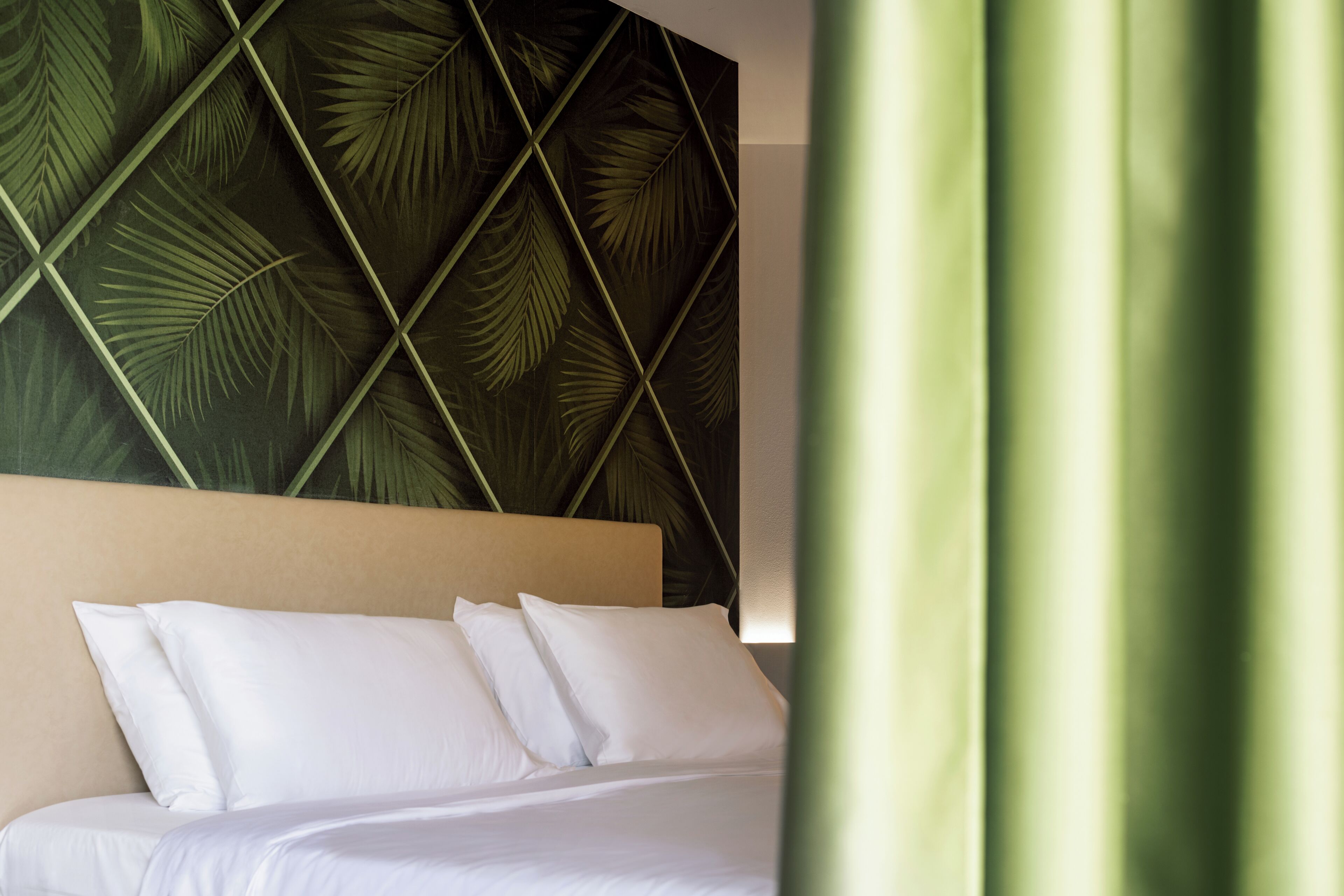 Ein Hotelzimmer mit Bett, weißer Bettwäsche und einer Wand mit geometrischem Blattmuster.