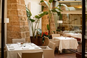 Interior de restaurante con paredes de piedra, plantas de interior y mesas dispuestas para comer.