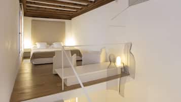 Una habitación de hotel moderna con techo de madera, cama con ropa blanca, sofá y una obra de arte original en la pared.