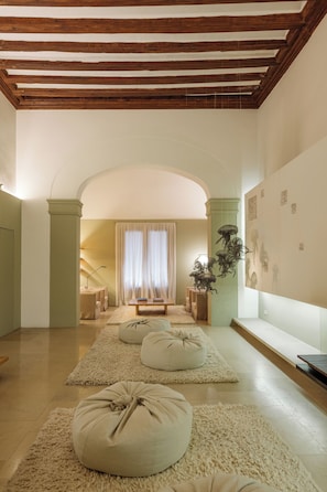 Un salón espacioso con techo alto, vigas de madera, un gran ventanal con cortinas y una obra de arte colgada en la pared.