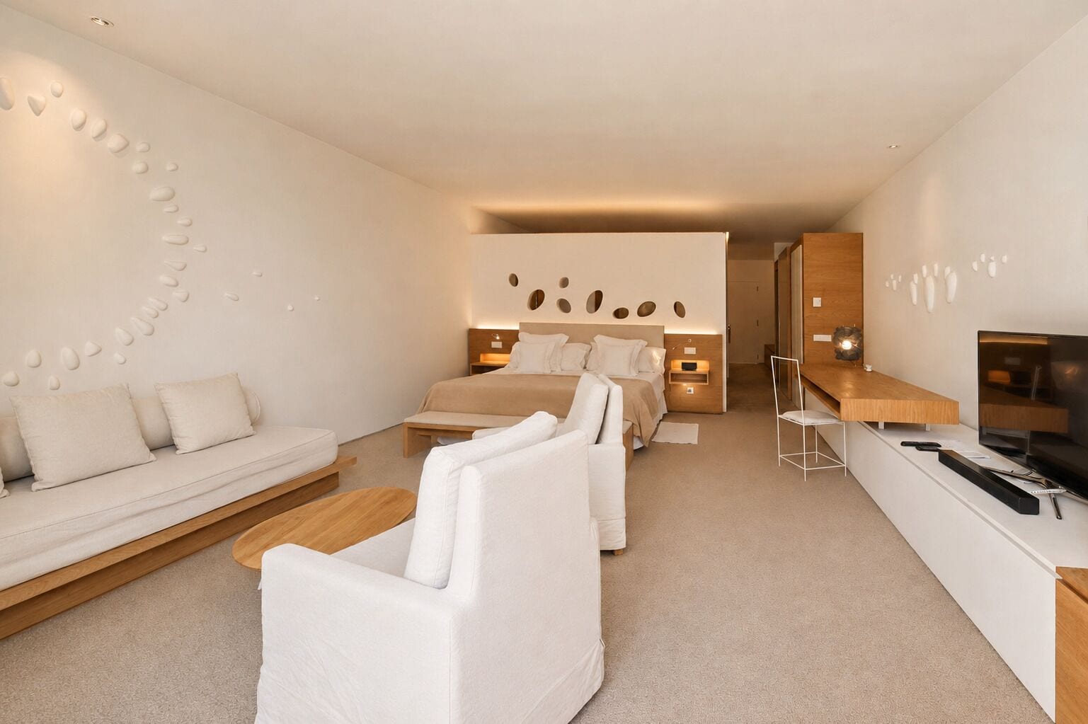 Una habitación de hotel moderna con sofá, dos camas, un televisor y una mesita de madera.
