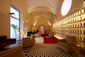 Un hall d'entrée avec un sol à carreaux, des canapés, une moquette rouge et un mur décoré de vases.