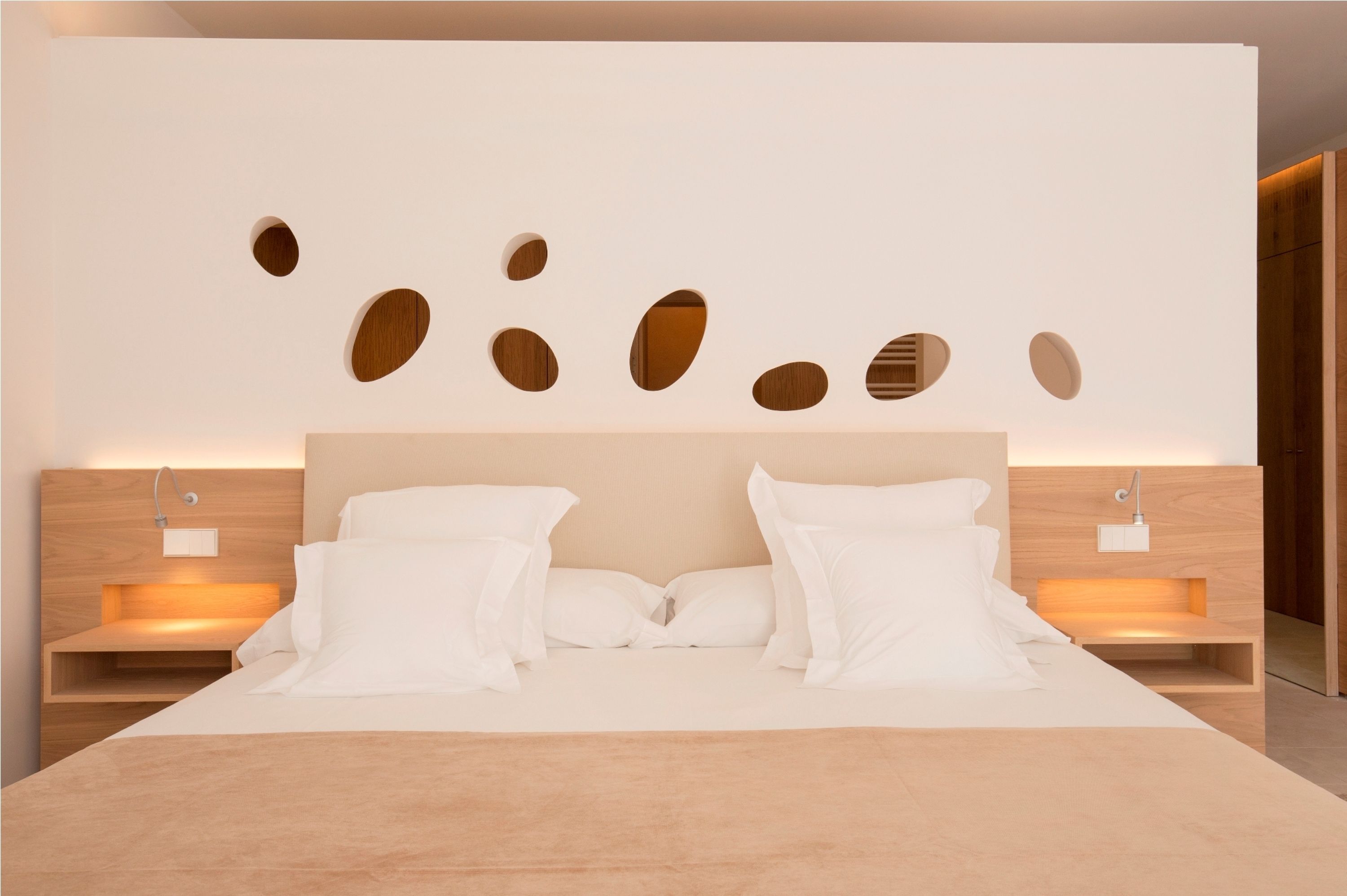 A modern bedroom with a large bed, wooden headboard, and wall-mounted light fixtures.
