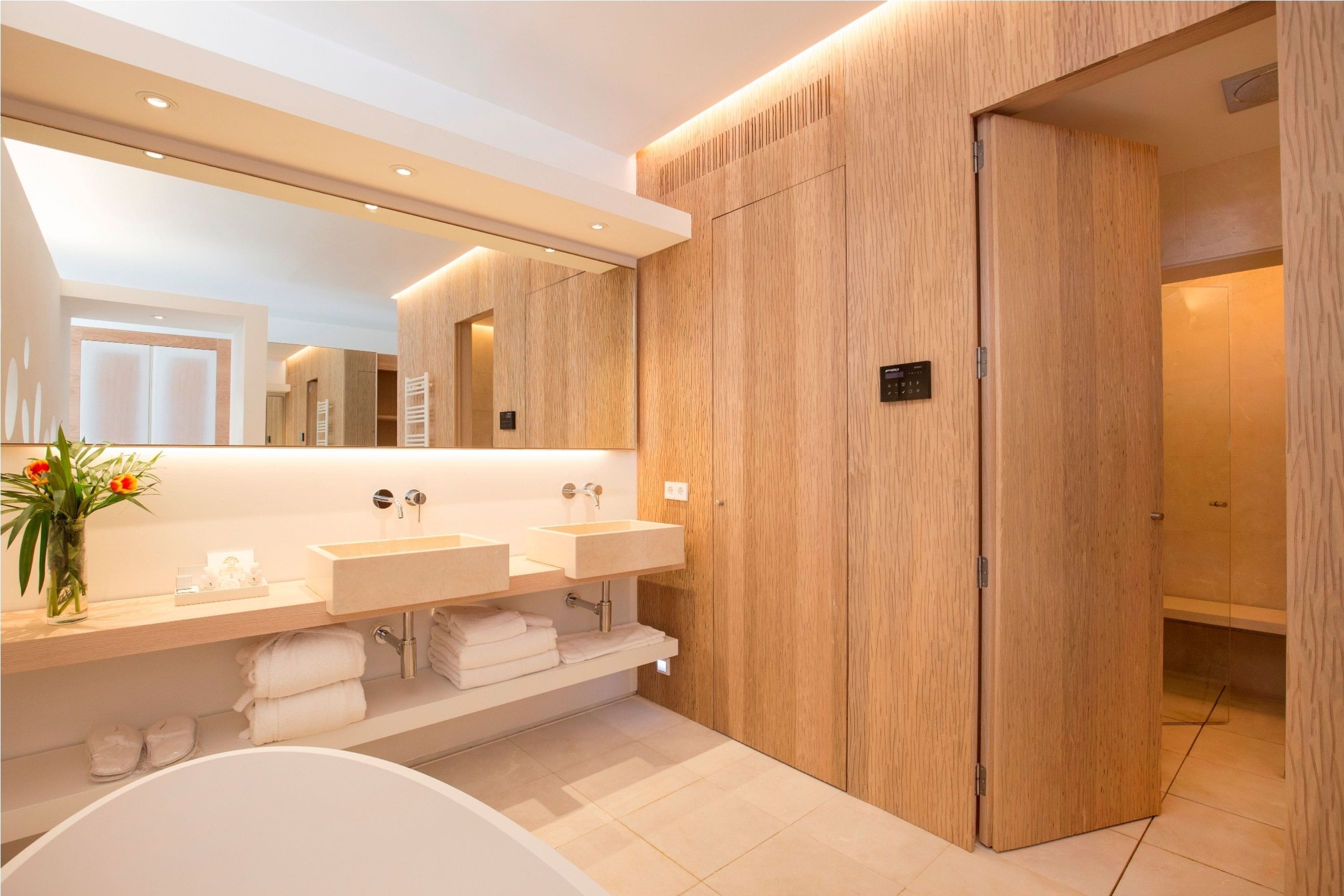 A modern bathroom with a large mirror, two sinks, a bathtub, and wooden paneling.