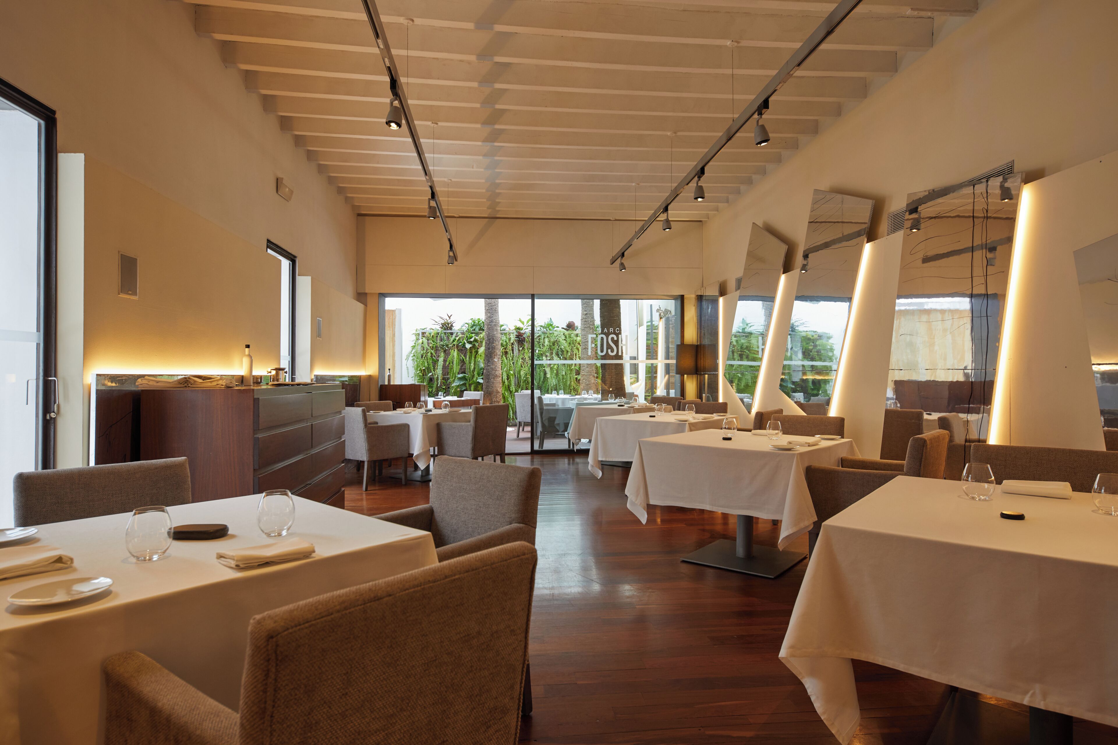 A restaurant with multiple tables, chairs, and a view of greenery outside.