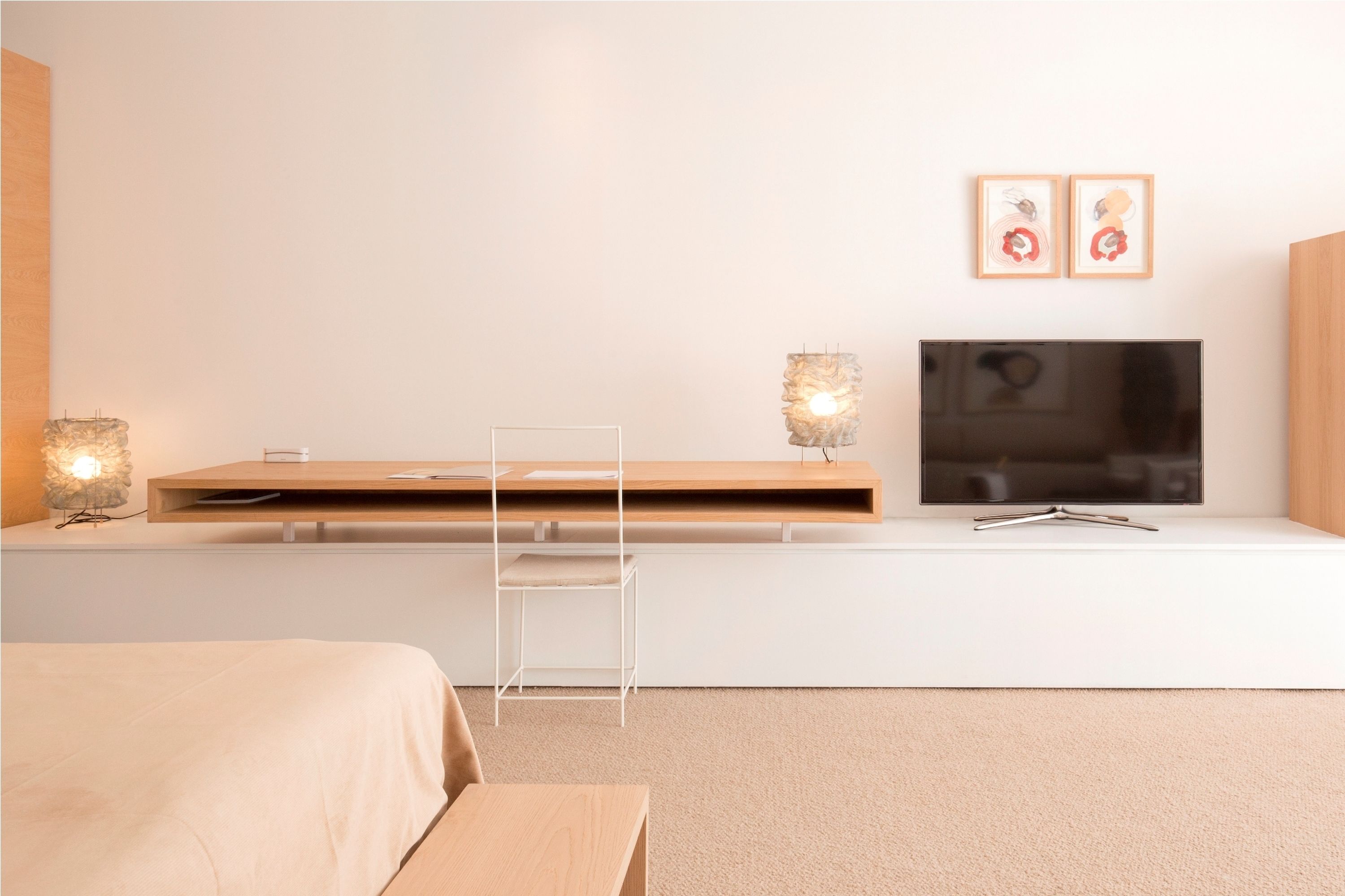 Un dormitorio moderno con cama, mesita de noche, lámpara, televisor y una obra de arte en la pared.