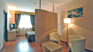 Habitación de hotel con escritorio, dos sillas, una cama, un cuadro en la pared y una lámpara.
