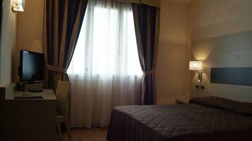 Quarto de hotel com cama, escrivaninha com computador, cadeira e televisão.