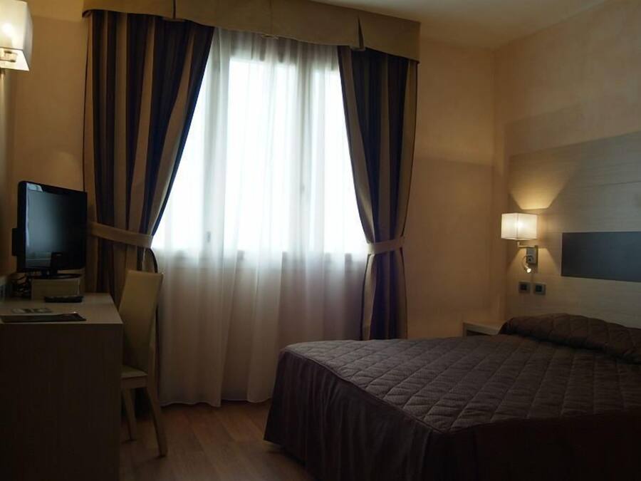 A hotel room with a bed, a desk with a computer, a chair, and a television.