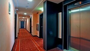 Un pasillo de hotel con alfombra roja, puertas y una lámpara en la pared.