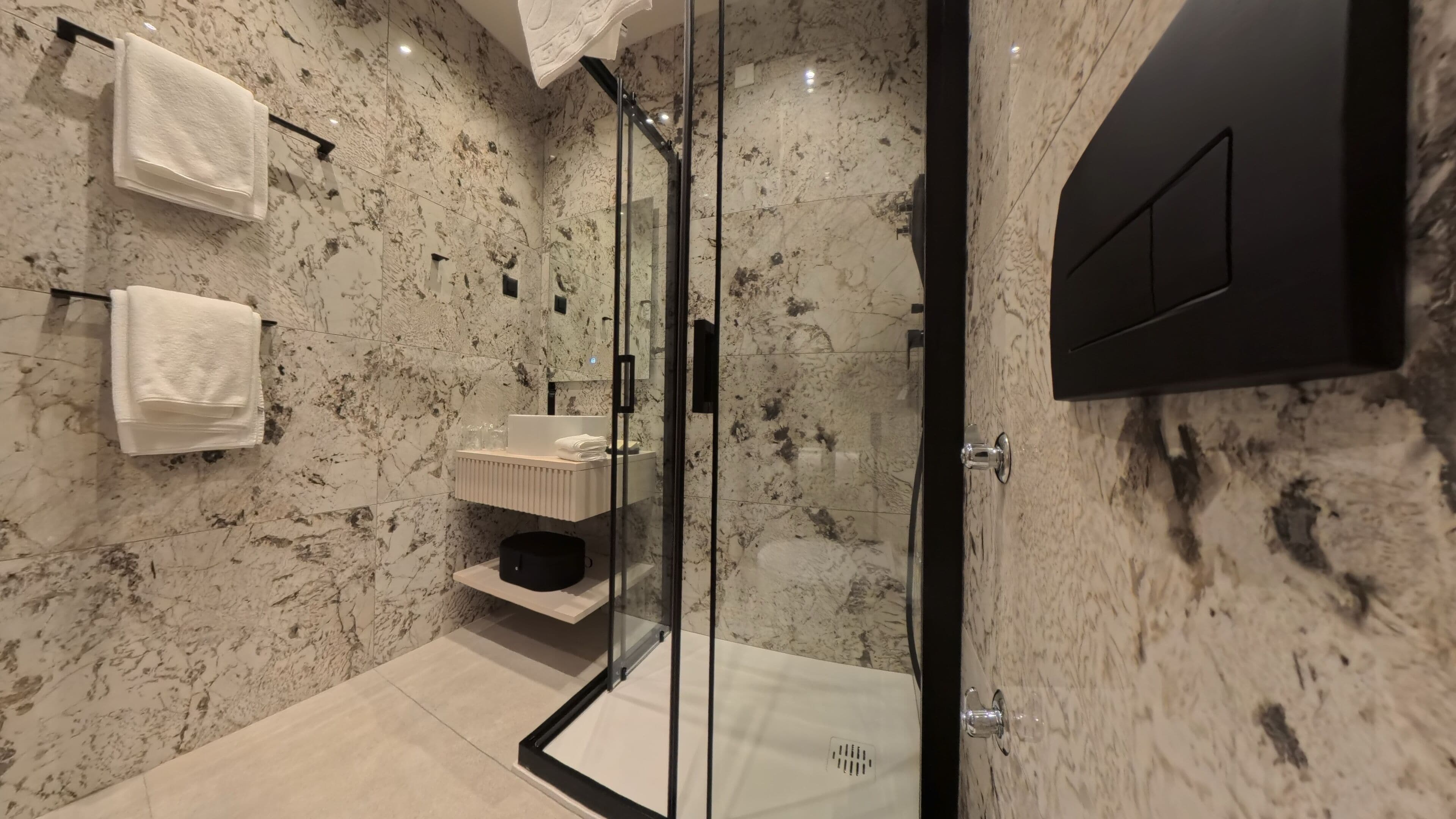 A modern bathroom with a glass-enclosed shower, marble walls, and a black door.