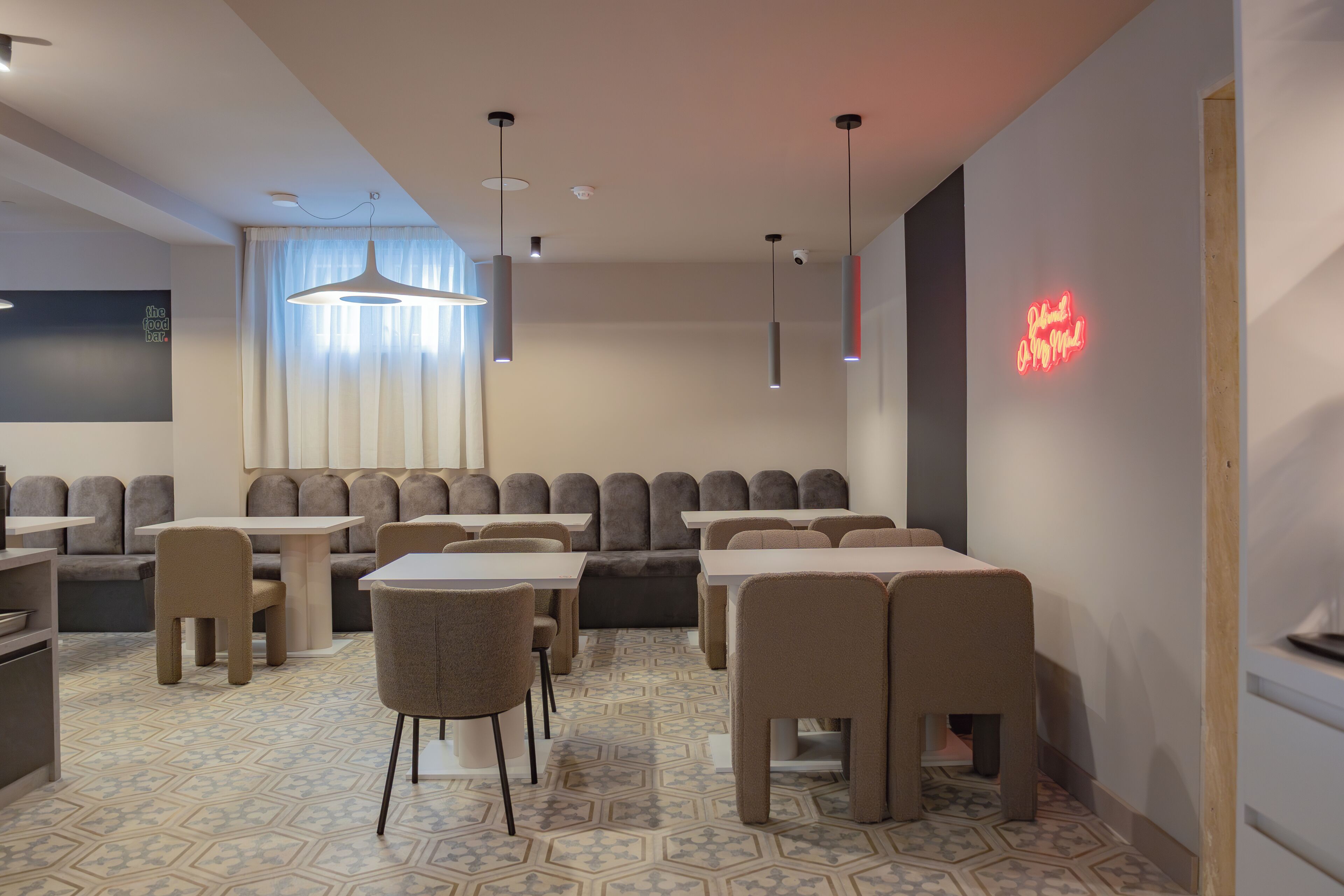 A modern restaurant with a geometric patterned floor, multiple seating areas including booths and tables, pendant lighting, and a neon sign on the wall.