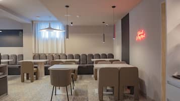 A modern restaurant with a geometric patterned floor, multiple seating areas including booths and tables, pendant lighting, and a neon sign on the wall.