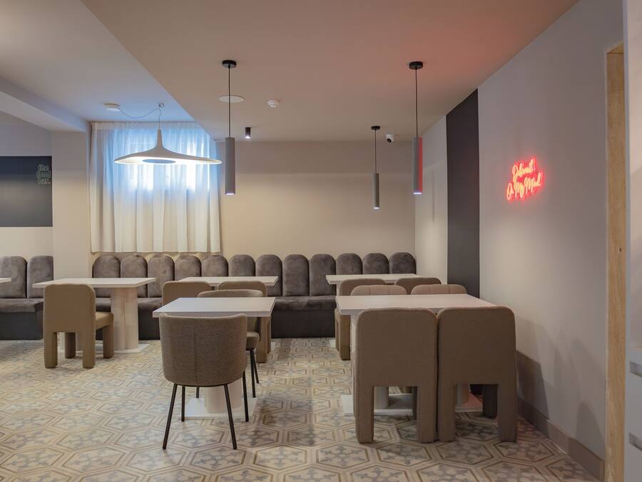 A modern restaurant with a geometric patterned floor, multiple seating areas including booths and tables, pendant lighting, and a neon sign on the wall.