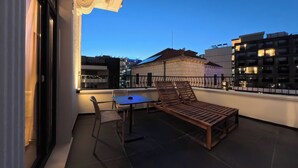 A balcony with a table and chairs, a wooden bench, and a view of buildings in the background. - Hotel Aquarius Adults Only (Dubrovnik)