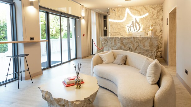 A modern living room with a curved sofa, a stone coffee table, and a large window offering a view of greenery. - Hotel Aquarius Adults Only (Dubrovnik)