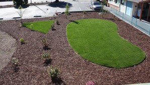 A landscaped area with a parking lot, a building with a blue facade, and a tree. - Budget Inn (San Luis Obispo)