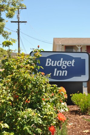 A sign for Budget Inn with a clear view of the surrounding area including a power line, some greenery, and a building in the background. - Budget Inn (San Luis Obispo)
