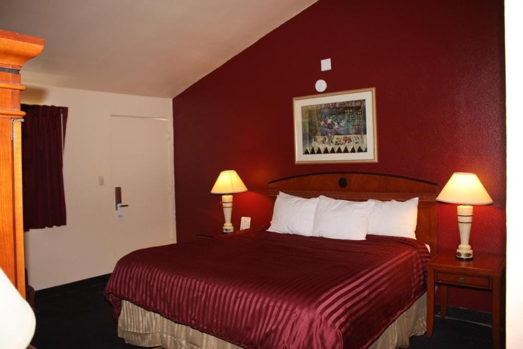 Une chambre d’hôtel avec un grand lit, deux lampes de chevet, une porte et un tableau encadré au mur.